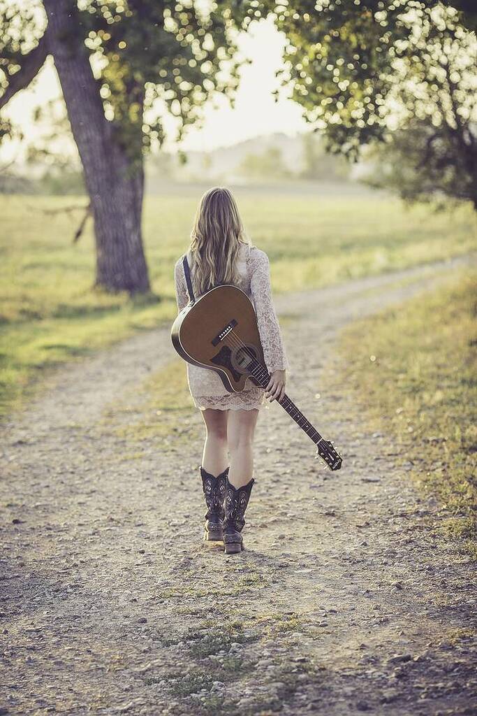 Jeune guitariste de dos sur un chemin de campagne.